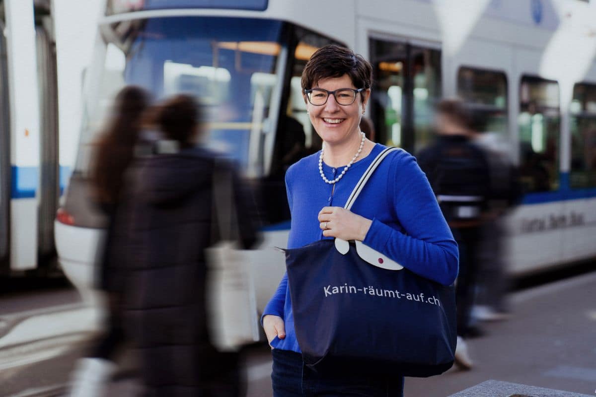 Frau in blauem Pulli und grosser Tasche steht vor einer Tram in Zürich